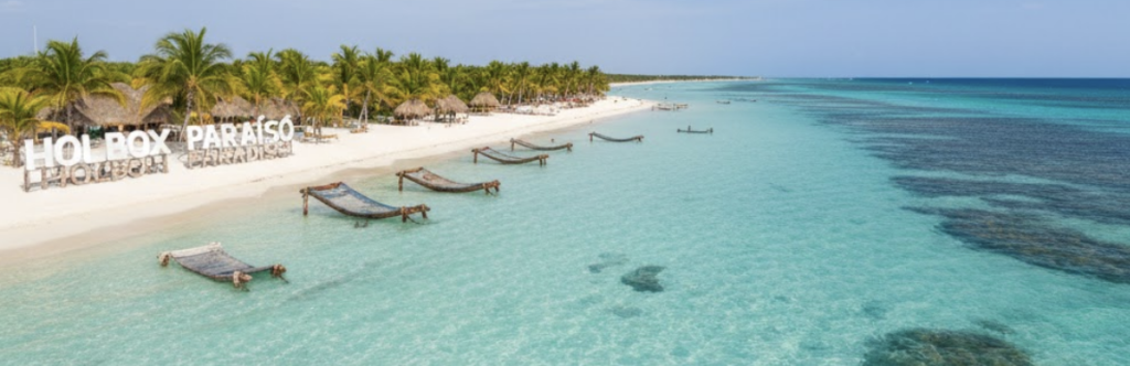 Hamacas sobre el agua cristalina de color turquesa en una playa de arena blanca en Holbox, México, con palmeras al fondo.